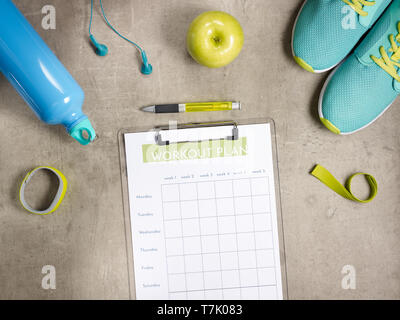 Closeup on green apple, headphones, elastic band, sneakers, fitness tracker, bottle of water and workout plan on clipboard with pen laying on the floo Stock Photo