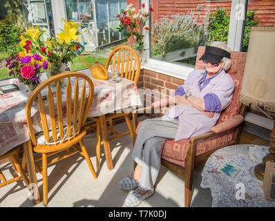 wearing sunglasses and a peaked cap to protect her eyes from the sun,a visually impaired 90 year old,with severe macular de-generation, sits in her su Stock Photo
