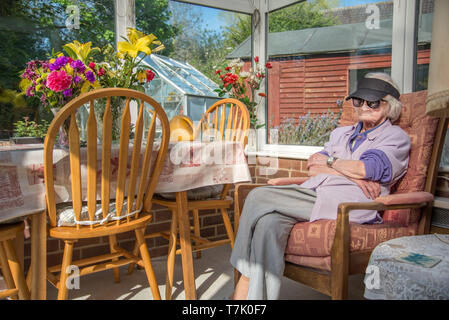 wearing sunglasses and a peaked cap to protect her eyes from the sun,a visually impaired 90 year old,with severe macular de-generation, sits in her su Stock Photo
