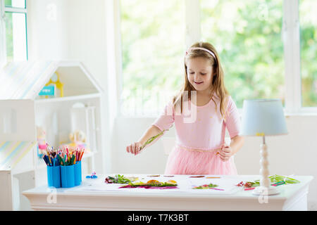 Child creating picture with colorful leaves. Art and crafts for kids. Little girl making collage image with rainbow plant leaf. Biology homework for y Stock Photo