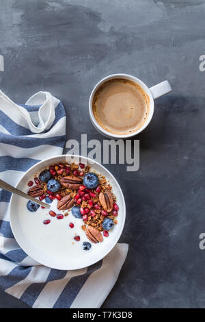 Homemade granola, muesli with pomegranate seeds, blueberries, pecan nuts and yogurt on gray concrete background. Healthy breakfast bowl. Top view. Stock Photo