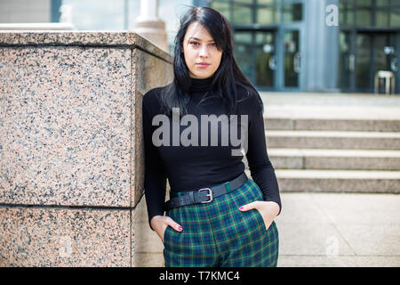 Young woman in black shirt and black hair standing in front of office building, half body, confidence Stock Photo