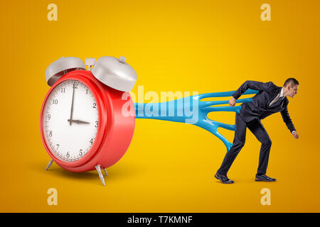 Young businessman stuck to red alarm clock with blue sticky slime on yellow background Stock Photo