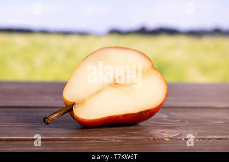 One half of fresh red pear with green wheat field Stock Photo