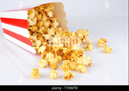 Overturned red and white tube with tasty caramel popcorn on white background. Snack and food concept. Stock Photo