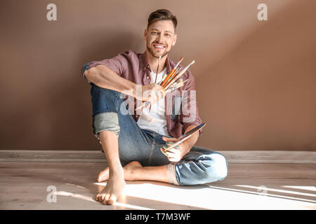 Male artist with paint tools and palette on floor near color wall Stock Photo