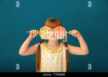 Cute little girl with lollipops on color background Stock Photo