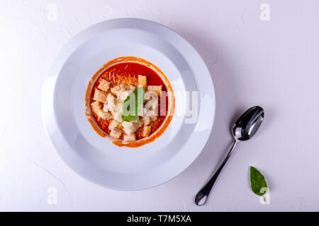 Tomato cream soup with crackers in a white plate on a white background. Stock Photo