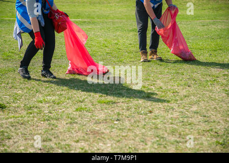 Man and woman volunteer wearing picking up trash and plastic waste in public park. Young people wearing gloves and putting litter into red plastic bag Stock Photo