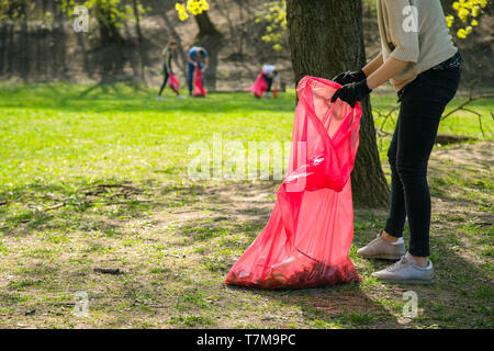 Man and woman volunteer wearing picking up trash and plastic waste in public park. Young people wearing gloves and putting litter into red plastic bag Stock Photo