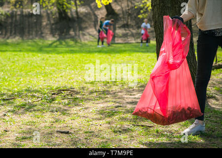 Man and woman volunteer wearing picking up trash and plastic waste in public park. Young people wearing gloves and putting litter into red plastic bag Stock Photo