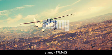 Small single engine airplane flying in the gorgeous sunset sky through the sea of clouds above the spectacular mountains Stock Photo