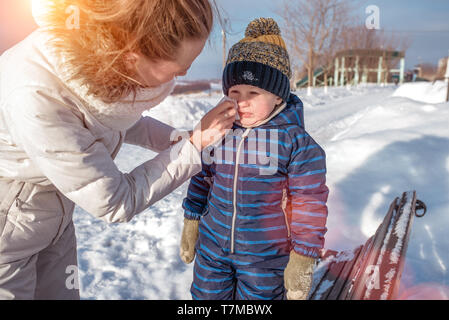 Mom wipes her nose with a napkin, her little boy's boy is 4 years old. In winter, on the nature, the background of the snow shop, rest in the winter Stock Photo