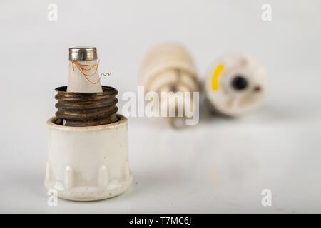 Old ceramic electric fuse. Blown and badly repaired security for energy, Bright background. Stock Photo