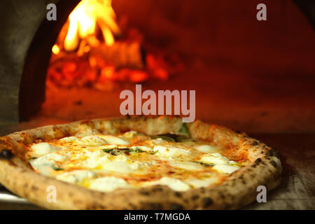 Tasty pizza near firewood oven in kitchen Stock Photo