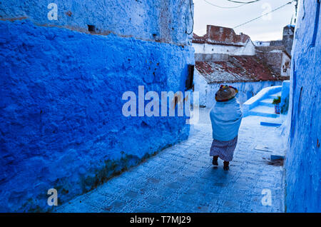 Chefchaouen, Morocco : A senior Riffian woman walks along a blue-washed alley in the medina old town. Stock Photo