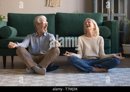 Happy mature couple having fun, practicing yoga together at home Stock Photo