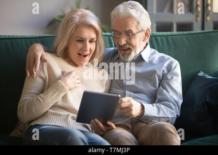 Surprised mature wife and husband using tablet, reading pleasant news Stock Photo