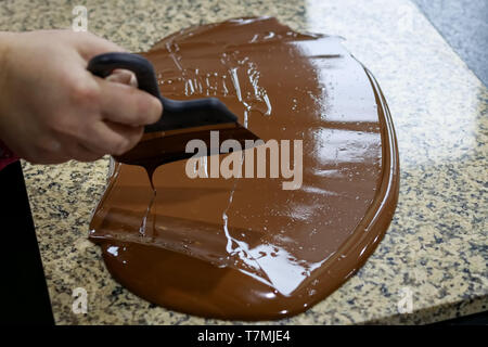 Chocolatier stirs the tempered chocolate on a granite table in order to cool Stock Photo