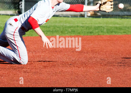 A shortstop dives fot the ball during a baseball game on a red turf infield Stock Photo