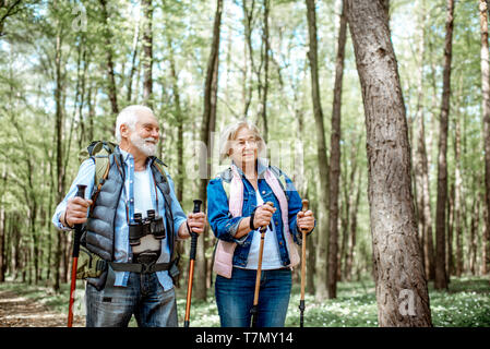 Beautiful senior couple hiking with backpacks and trekking sticks in the forest. Concept of active lifestyle on retirement Stock Photo