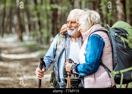 Lovely senior couple hugging in the forest while hiking with backpacks and trekking sticks. Concept of active lifestyle on retirement Stock Photo