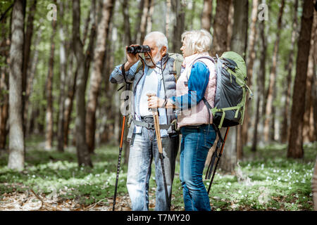Senior couple looking with binoculars while hiking in the forest. Concept of an active lifestyle on retirement Stock Photo