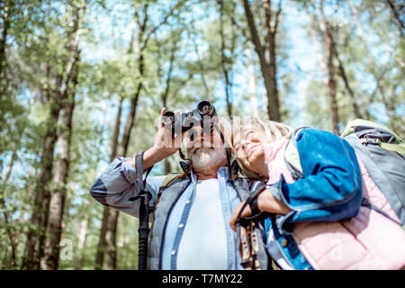 Senior couple looking with binoculars while hiking in the forest. Concept of an active lifestyle on retirement Stock Photo