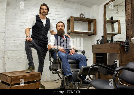 Barbershop, hairdresser and client. Hairdresser and bearded young guy posing for the camera before a haircut. Stock Photo