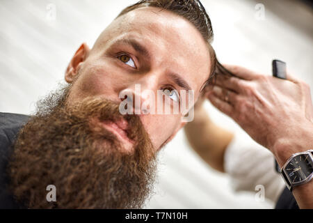 Stylish barber cuts a brutal man with a thick beard. Stock Photo