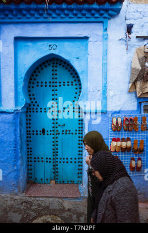 Chefchaouen, Morocco : Two women walk past a traditional wooden door in the blue-washed medina old town. Stock Photo