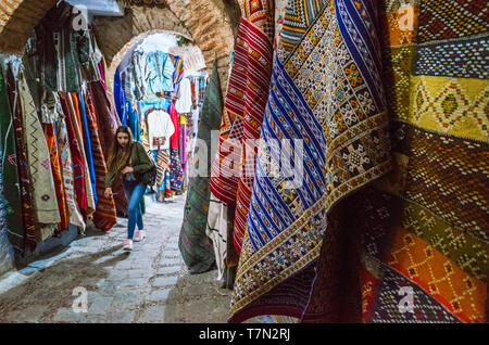 Chefchaouen, Morocco : A young woman walks under an arch past handwoven carpets for sale in the medina old town. Stock Photo