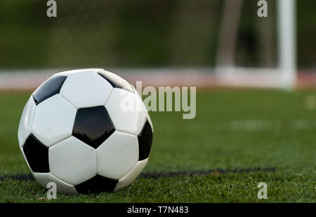 A black and white soccer or football on green field with goal or net in background Stock Photo