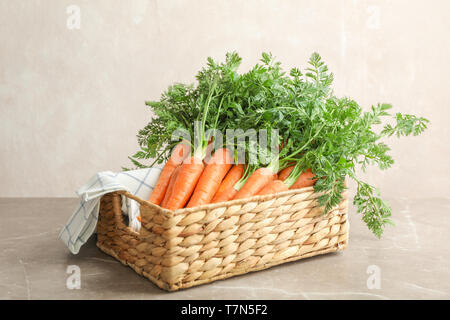 Wicker basket with ripe carrots on grey table against light background Stock Photo