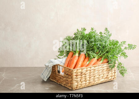 Wicker basket with ripe carrots on grey table against light background Stock Photo