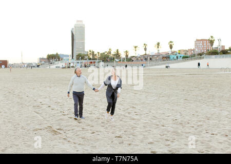 Senior happy caucasian husband and wife running on sand beach and holding hands. Concept of happy couple and health way of life. Stock Photo