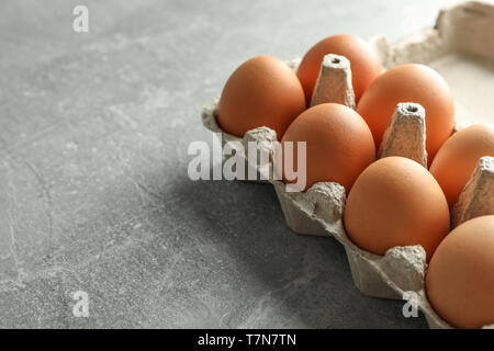 Chicken eggs in carton box on gray background, space for text Stock Photo