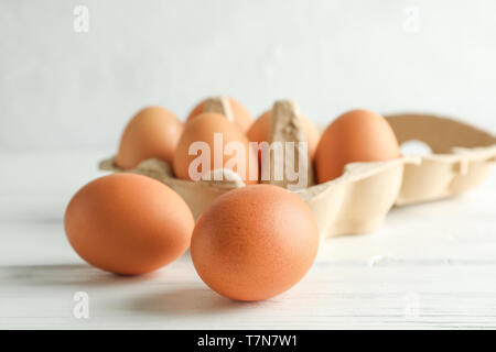 Chicken eggs in carton box on wooden table against white background Stock Photo