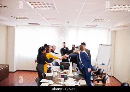 Multiracial business people standing at office and put hands on hands. Diverse group of employees in formal wear. Stock Photo