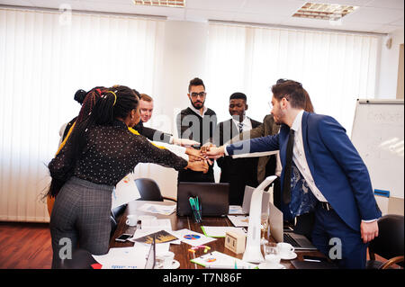 Multiracial business people standing at office and put hands on hands. Diverse group of employees in formal wear. Stock Photo