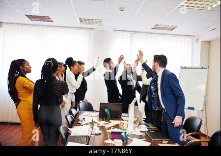 Multiracial business people standing at office and give high five each other. Diverse group of employees in formal wear. Stock Photo