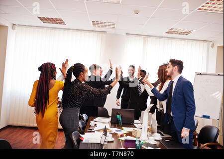 Multiracial business people standing at office and give high five each other. Diverse group of employees in formal wear. Stock Photo