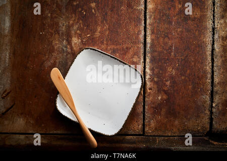 Empty square butter dish or bread plate with a wooden spreader over the corner on a rustic wood table viewed from overhead with copy space for product Stock Photo