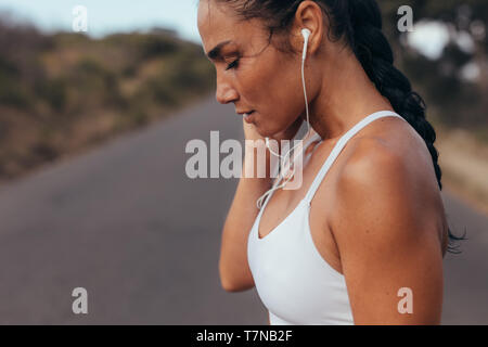 Side view of a female athlete wearing earphones listening to music while on training session. Sportswoman listening to music outdoors in morning. Stock Photo