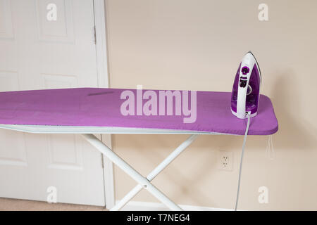 Closeup of home iron on purple board in bedroom room with nobody against wall Stock Photo