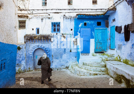 Chefchaouen, Morocco : A Moroccan woman walks past blue-washed traditional buildings in the medina old town. Stock Photo