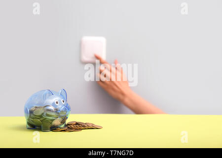 Piggy bank with coins and female hand turning on light by using switch on wall. Electricity saving concept Stock Photo