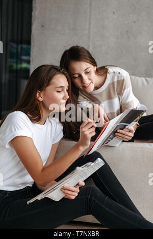 Two smiling teenage girls reading magazines while sitting on a couch at home Stock Photo