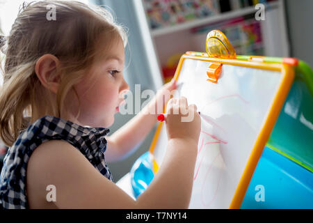 A four year old girl practices her handwriting on a whiteboard
