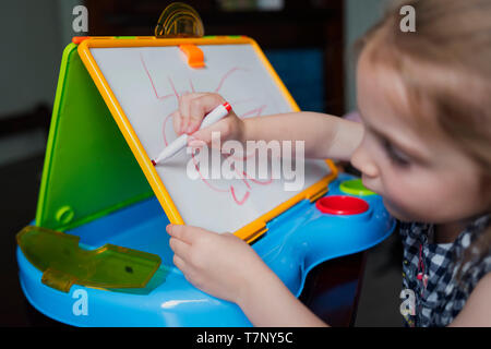 A four year old girl practices her handwriting on a whiteboard
